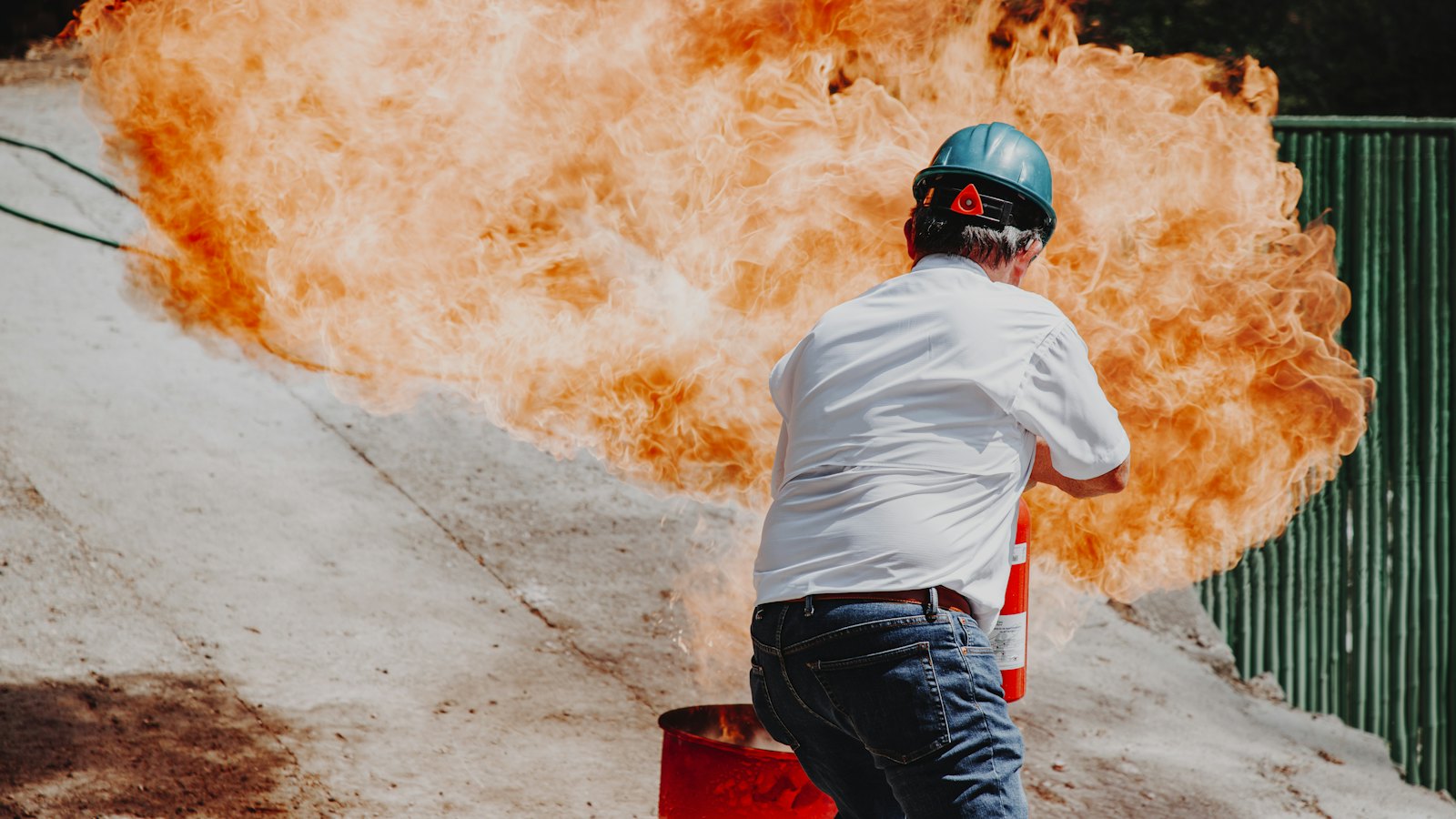 Löschübung: Ein Mann mit Schutzhelm steht vor einer großen Flamme auf dem Übungsplatz