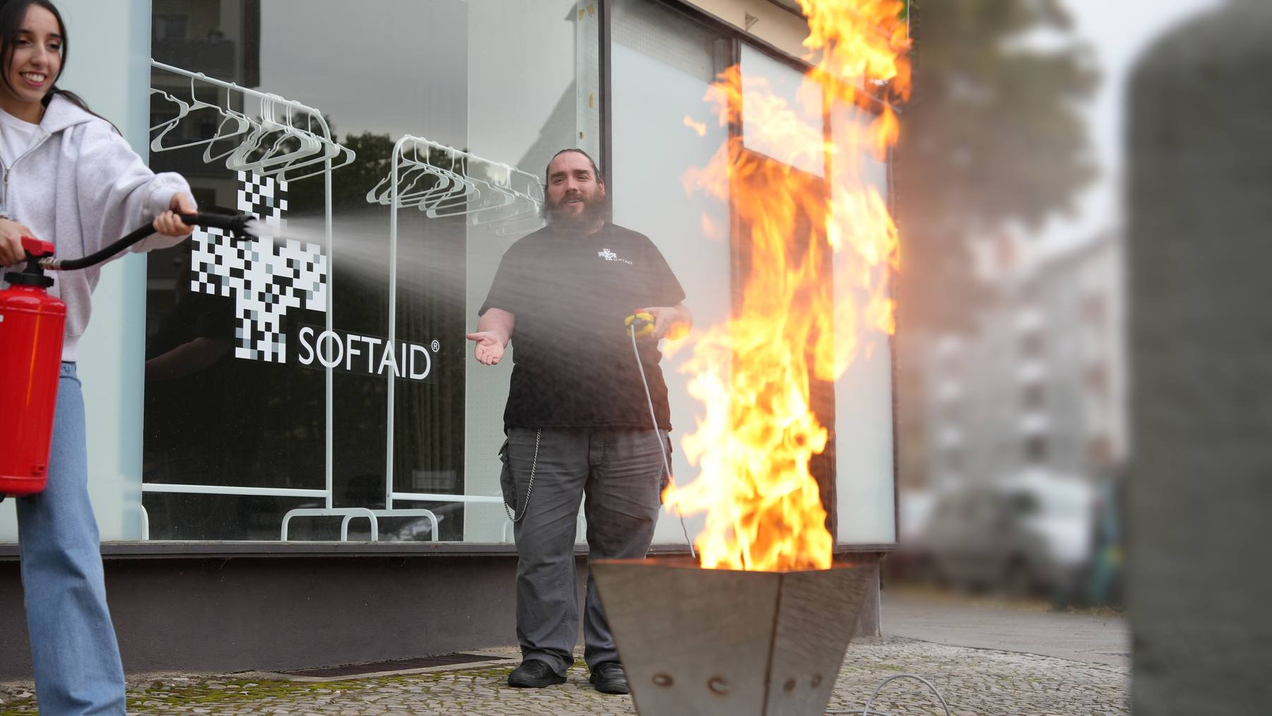Löschübung bei SoftAid: Eine Teilnehmerin löscht mit dem Feuerlöscher, der Trainer steuert den Brandsimulator