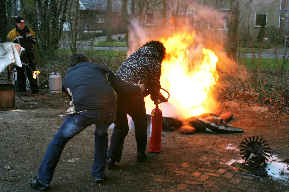 Zwei Personen in Alltagskleidung löschen ein Übungsfeuer mit dem Feuerlöscher